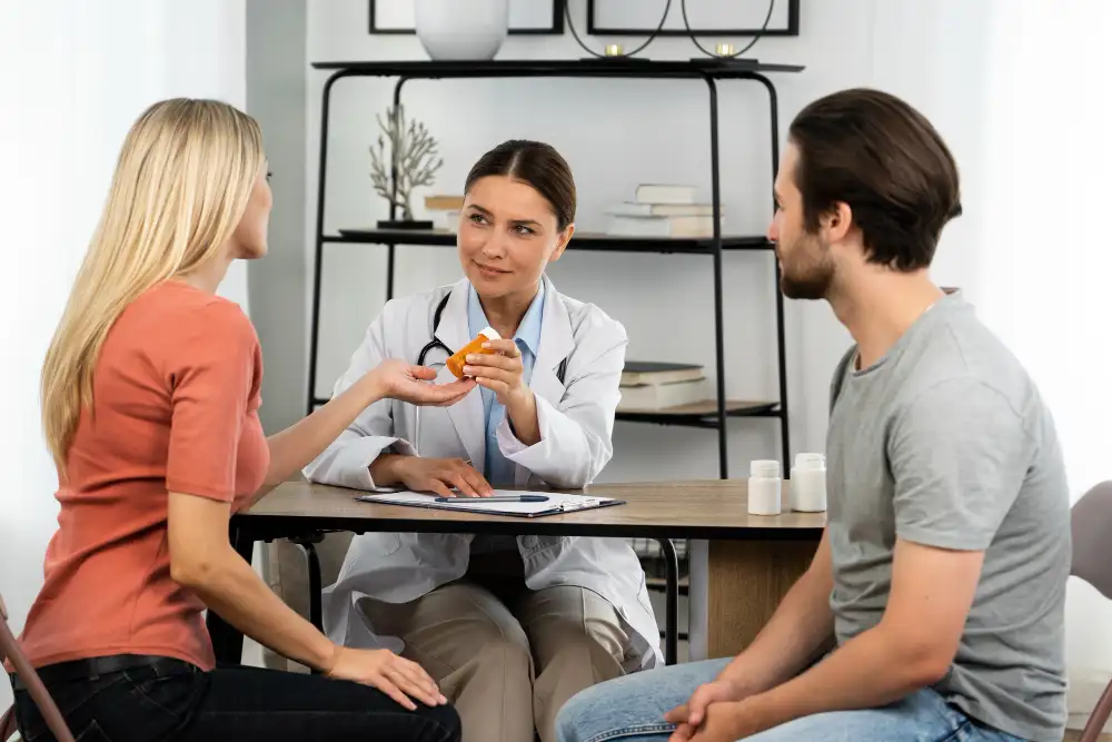 Female doctor consulting with couple and handing prescription medication during clinic visit
